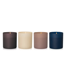 Four matte cylindrical candles in dark brown, cream, taupe, and navy blue, arranged in a row on a white background.