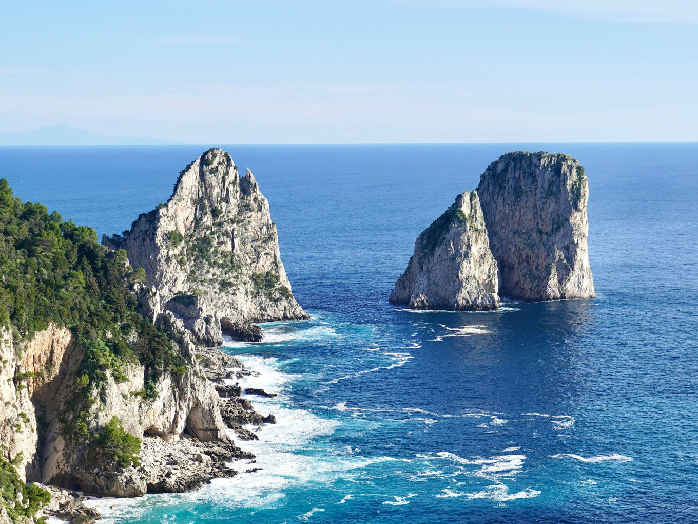 Two large rock formations in the ocean with a clear blue sky.