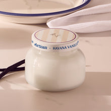 Jar of Artisan Havana Vanilla cream on a beige surface with a vanilla bean visible.