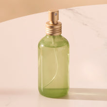 Green spray bottle with gold nozzle on a beige background