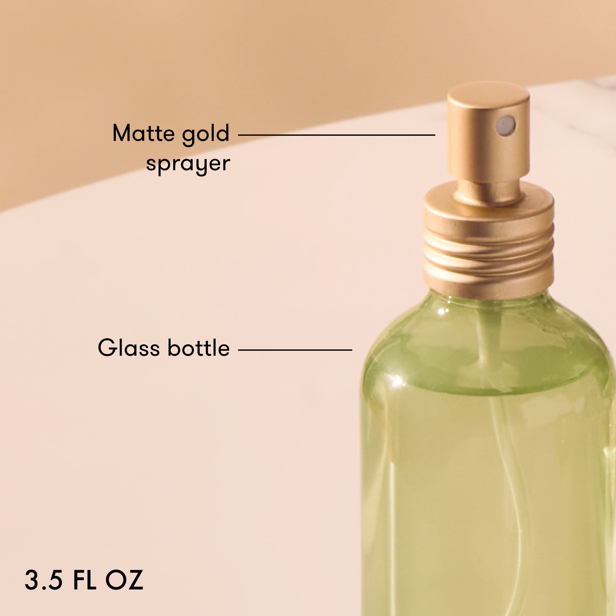 Green glass bottle with matte gold sprayer on a beige background