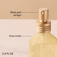 Glass bottle with matte gold sprayer labeled on a beige background