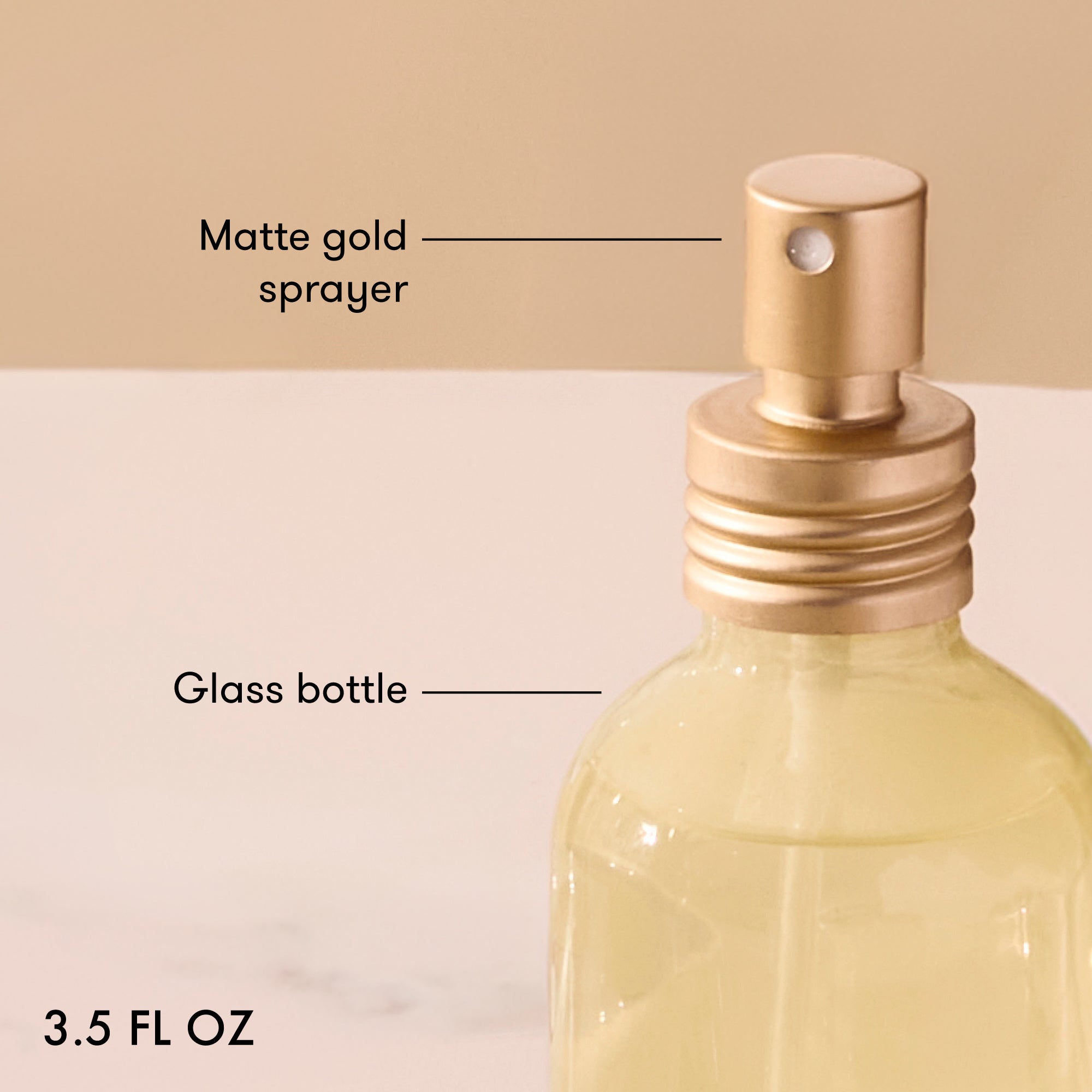 Glass bottle with matte gold sprayer labeled on a beige background