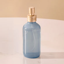 Blue spray bottle with gold nozzle on a light surface