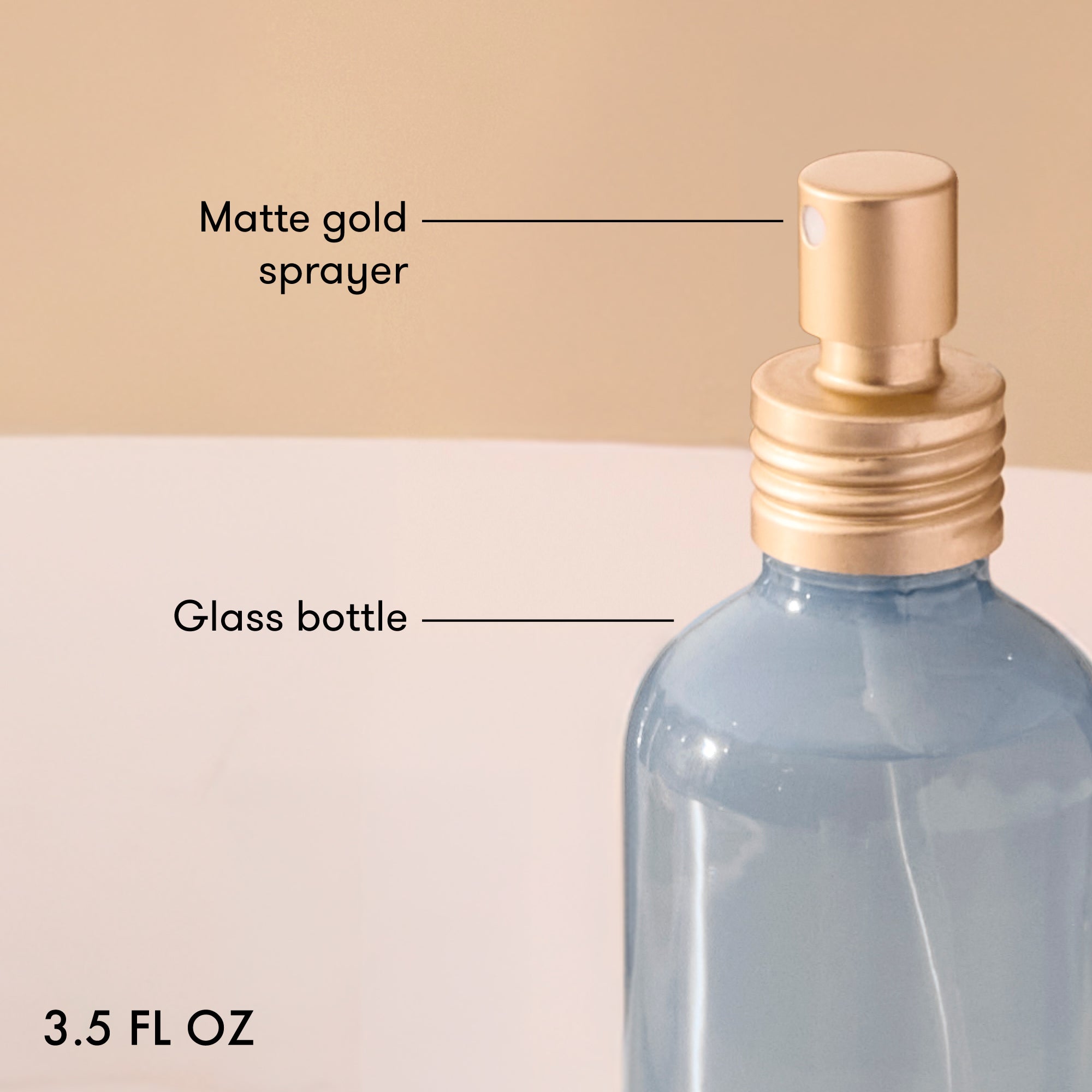 Glass bottle with matte gold sprayer labeled on a beige background