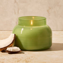 Green ceramic jar with a candle inside on a wooden surface with a light background