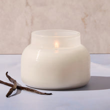 White candle in a textured jar with a branch on a light background