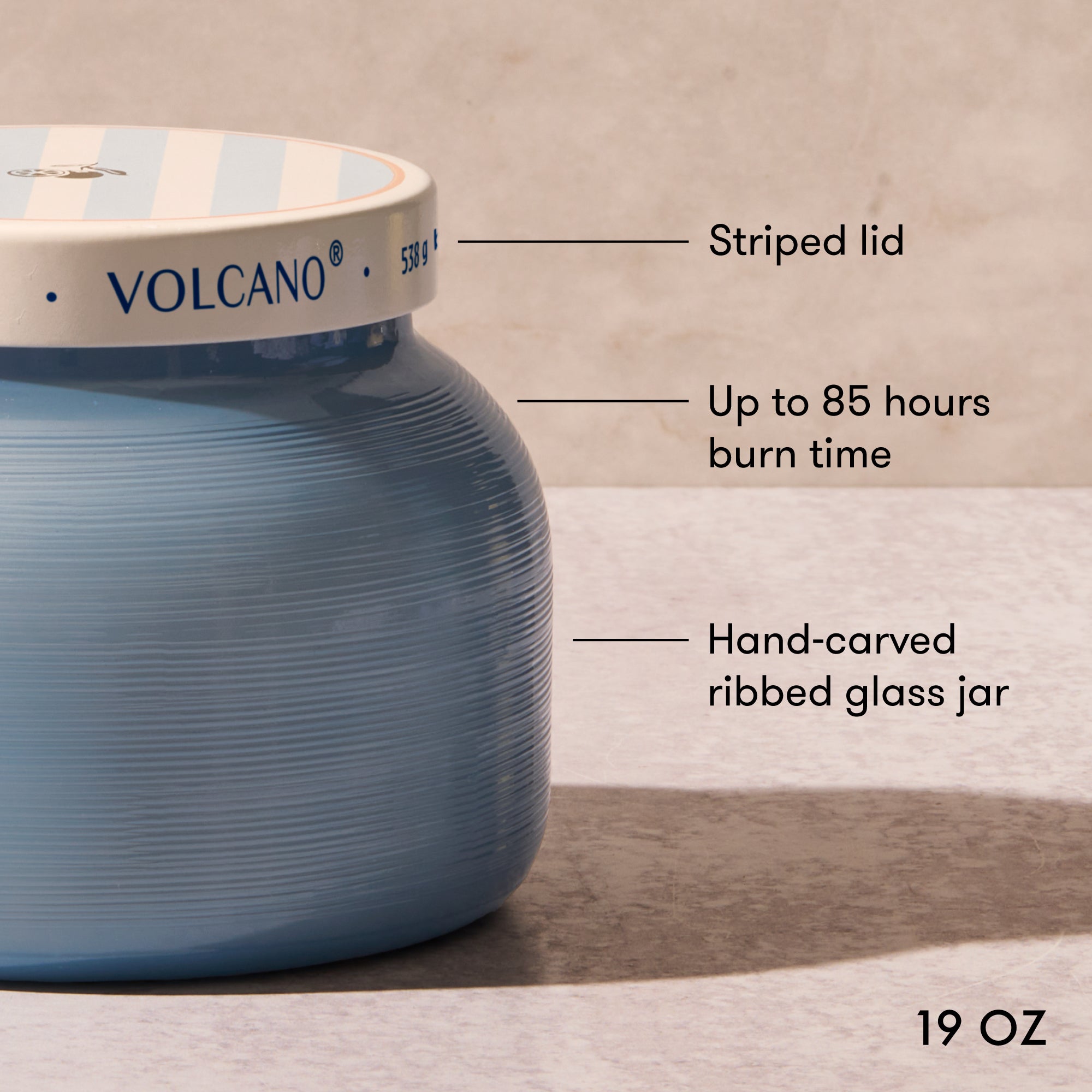 Blue glass jar with striped lid labeled 'Volcano', featuring text on burn time and size.