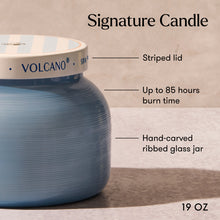 Blue candle with striped lid labeled 'Volcano' on a wooden surface