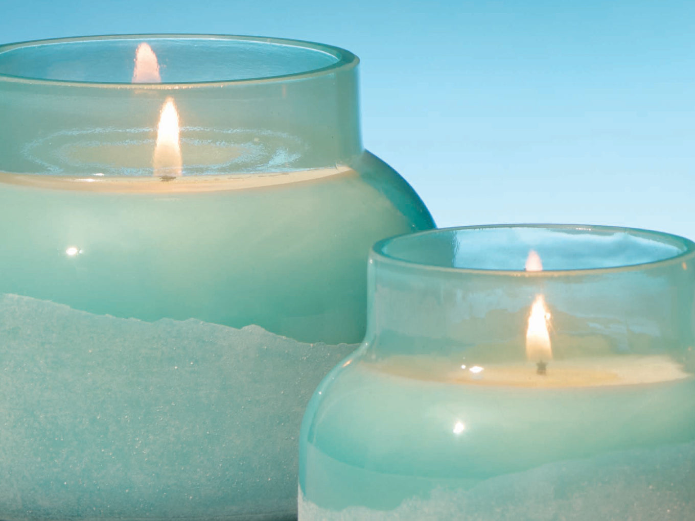 Two teal glass candles with flames on a light blue background