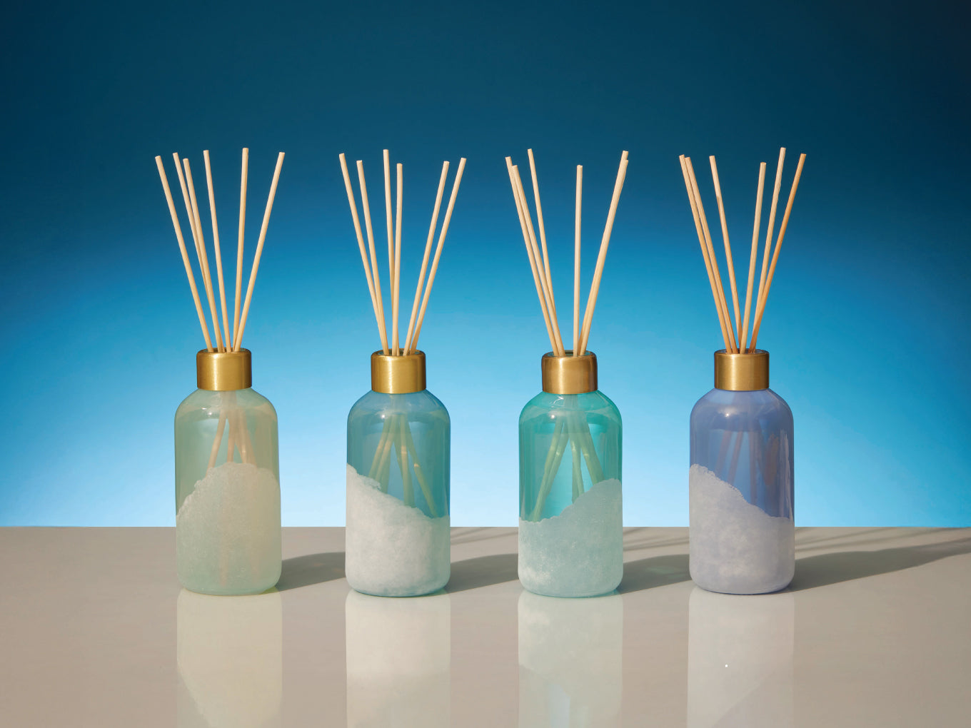 Four diffuser bottles with reeds against a blue gradient background