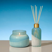 Candle and diffuser set with blue and white design on a reflective surface and blue background