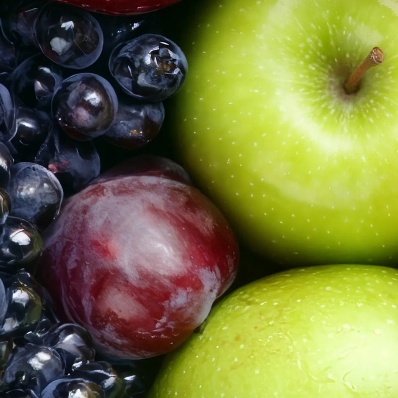Close-up of fresh fruit including two green apples and a red-purple plum, filling the frame.