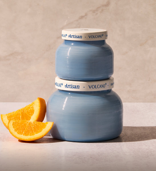 Two blue ceramic pots with 'Artisan Volcano' branding next to an orange slice on a neutral background