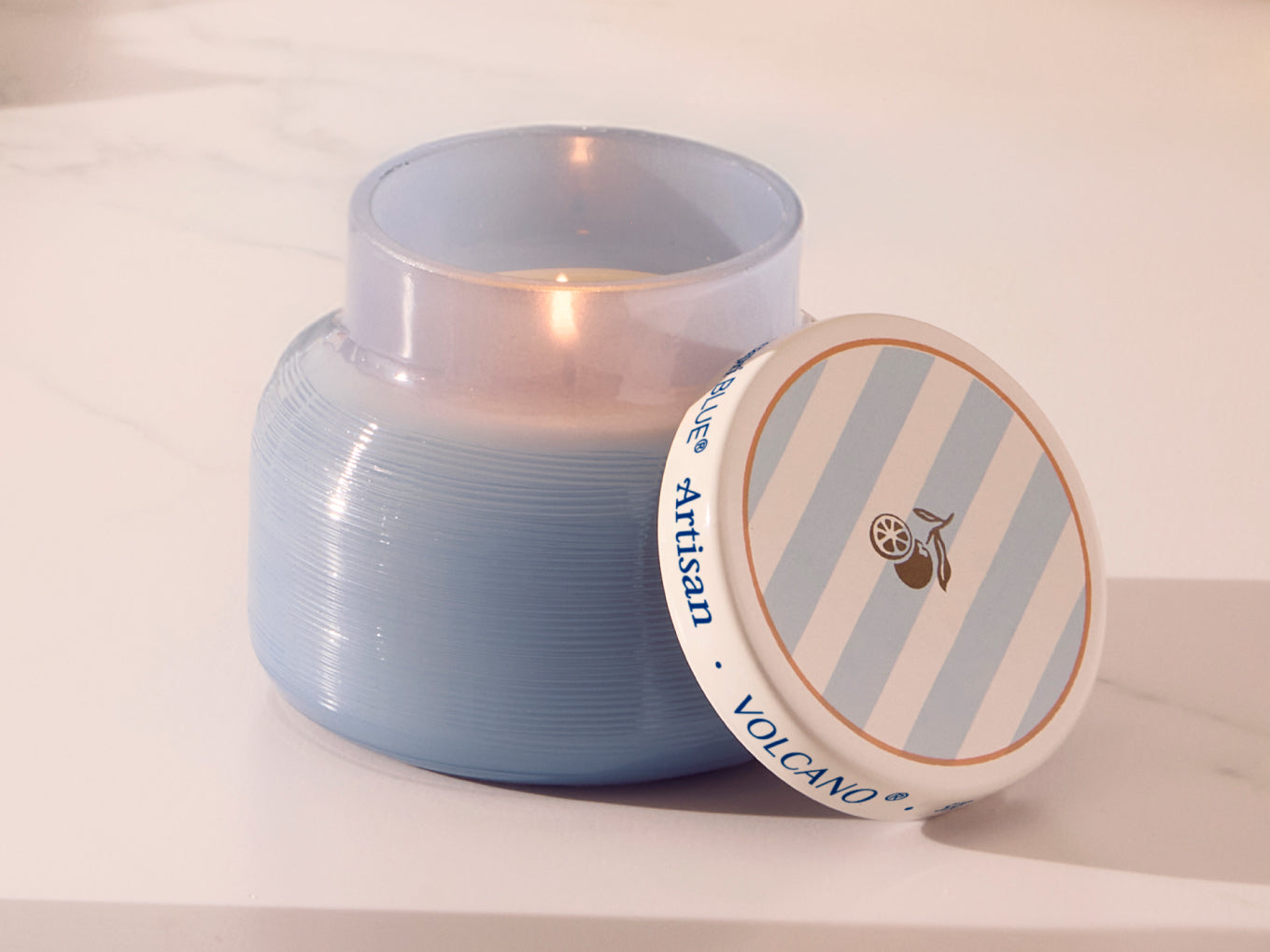 Blue candle in a glass jar with a striped lid on a white surface