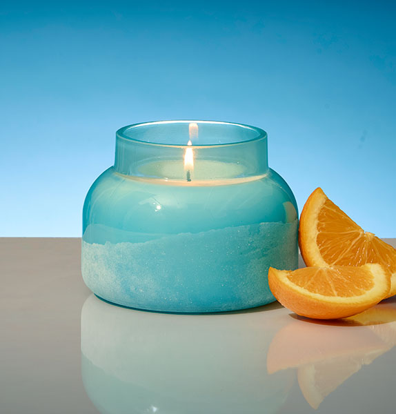 Blue candle in a glass jar with orange slices on a reflective surface and blue background