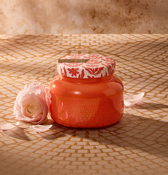 Red candle with floral lid on a textured surface with a pink rose.