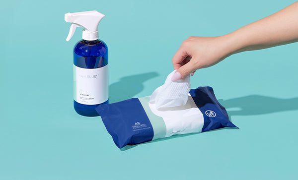 Hand reaching for a cleaning wipe from a packet next to a spray bottle on a teal background