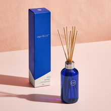 Blue capri BLUE diffuser bottle with reeds and packaging on a pink background