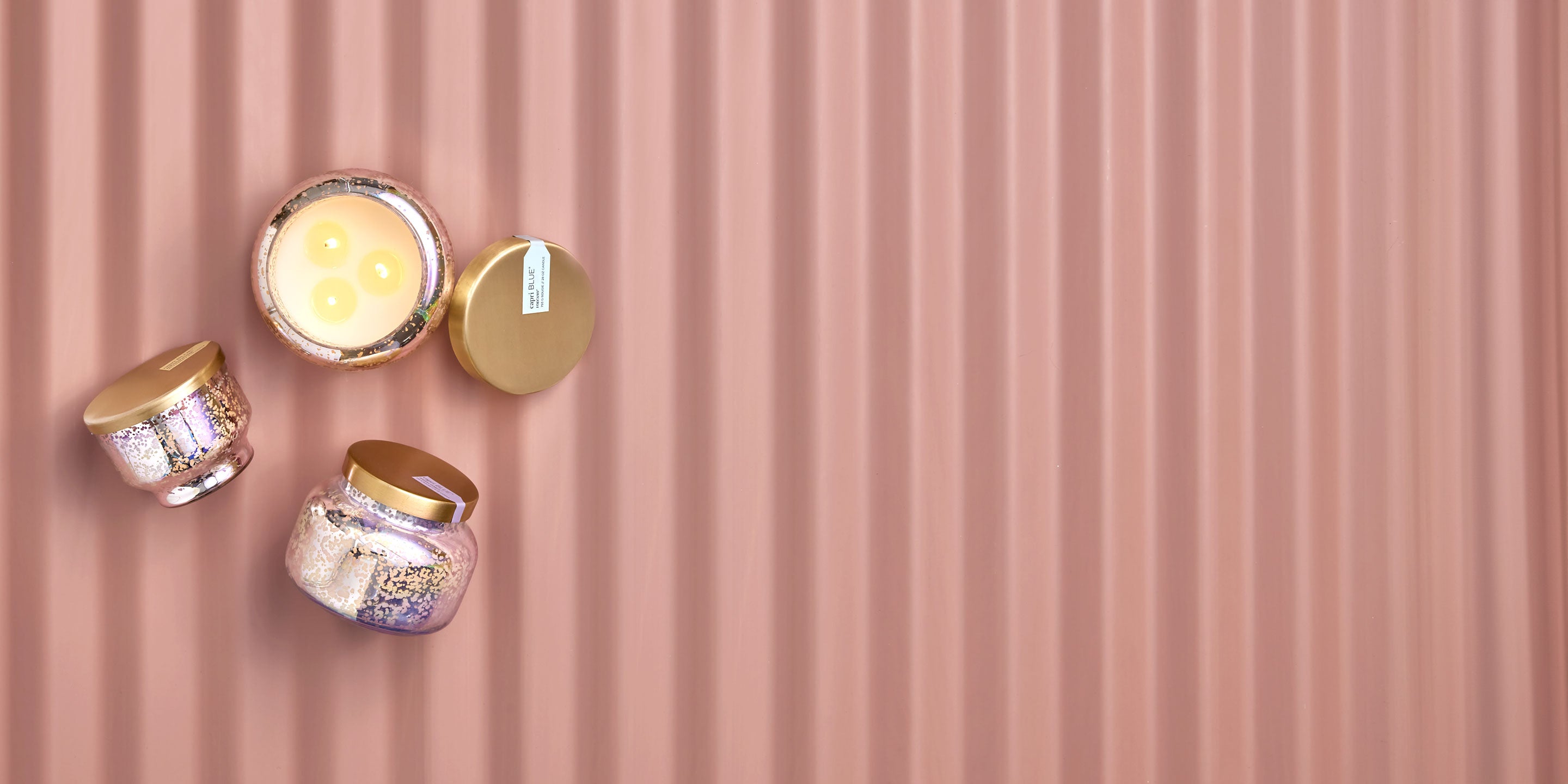Four candles in decorative tins on a pink corrugated background