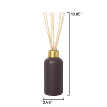 A reed diffuser bottle in dark brown with a gold collar and natural wood reeds, shown with dimension lines indicating a height of 10.85 inches and a base width of 2.