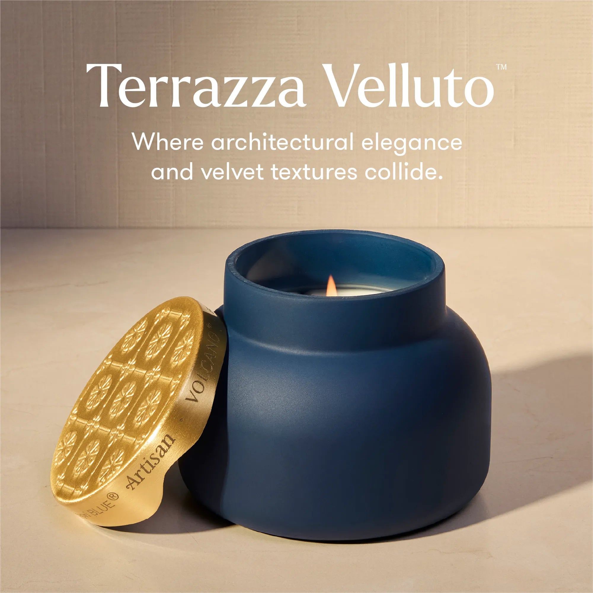 Terrazza Velluto scented candle in a matte navy blue jar with a gold lid resting beside it on a beige surface against a textured beige wall. White text at the top reads 'Terrazza Velluto' and 'Where architectural elegance and velvet textures collide.