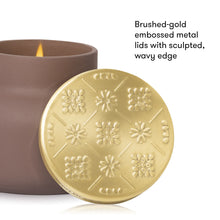 A close-up of a candle jar with a brushed gold embossed metal lid leaning in front, next to the brown candle container. Text on the right reads: 'Brushed-gold embossed metal lids with sculpted, wavy edge.