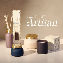 A curated product lineup from capri BLUE Artisan featuring a reed diffuser, a candle, a jar candle, and boxes, styled on a light surface against a warm beige background with the brand name 'capri BLUE Artisan' displayed in white text.