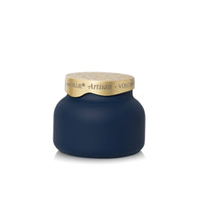 A New Blue Artisan Volcano candle in a rounded matte navy blue jar with a textured gold lid, shown on a clean white background.