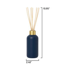 A reed diffuser bottle in matte navy blue with a gold collar and natural beige reeds, shown on a white background with dimension lines indicating height of 10.85 inches and width of 2.