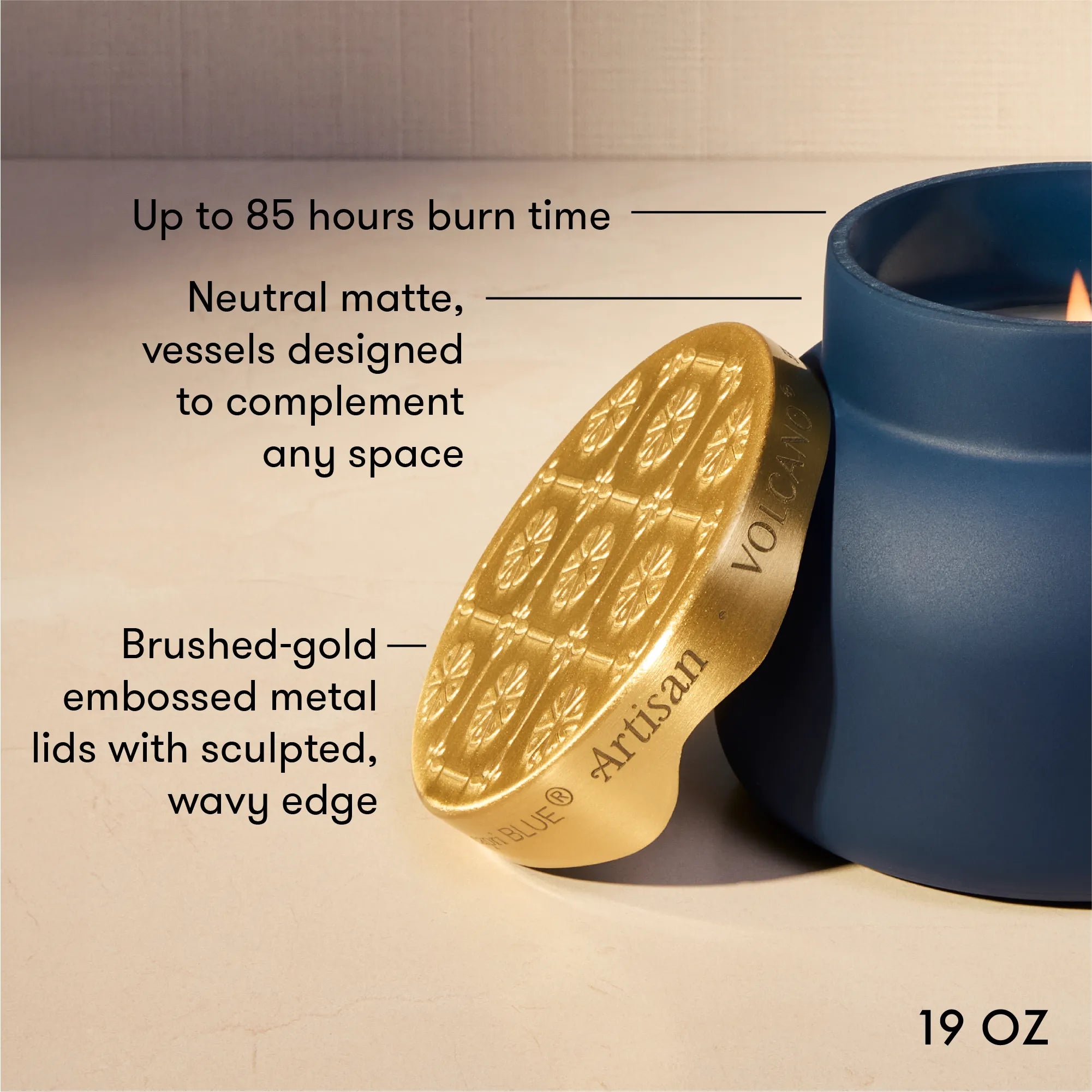 A 19 oz scented candle wax melt by Artisan Volatility, shown with its brushed gold metal lid leaning against a blue ceramic container. The image includes text callouts highlighting features like up to 85 hours of burn time, neutral matte vessels, and the brushed-gold embossed lid.