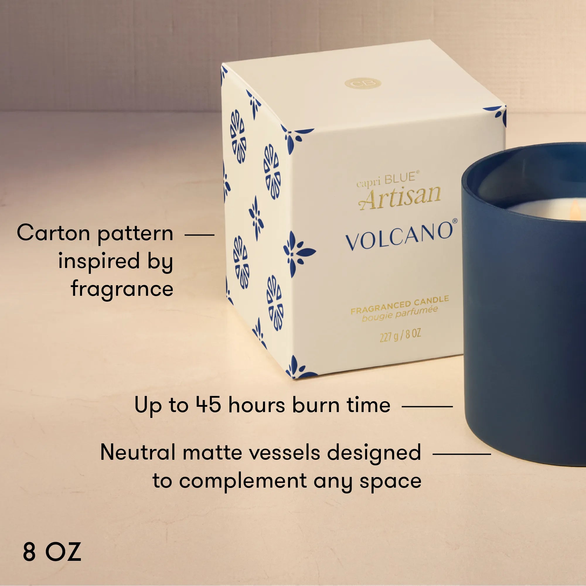 A 3D-rendered product presentation of a Volcano Artisan scented candle by Capri Blue. The product features a white square box with blue floral patterns and gold lettering, next to a matte navy blue cylindrical vessel.