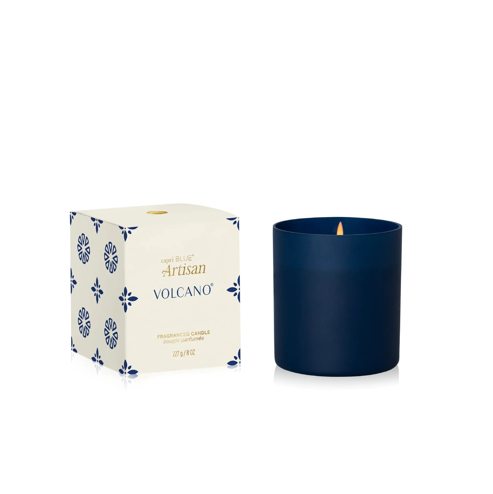 A navy blue glass candle jar next to its cream-colored packaging box with blue floral patterns and gold lettering, on a clean white background.