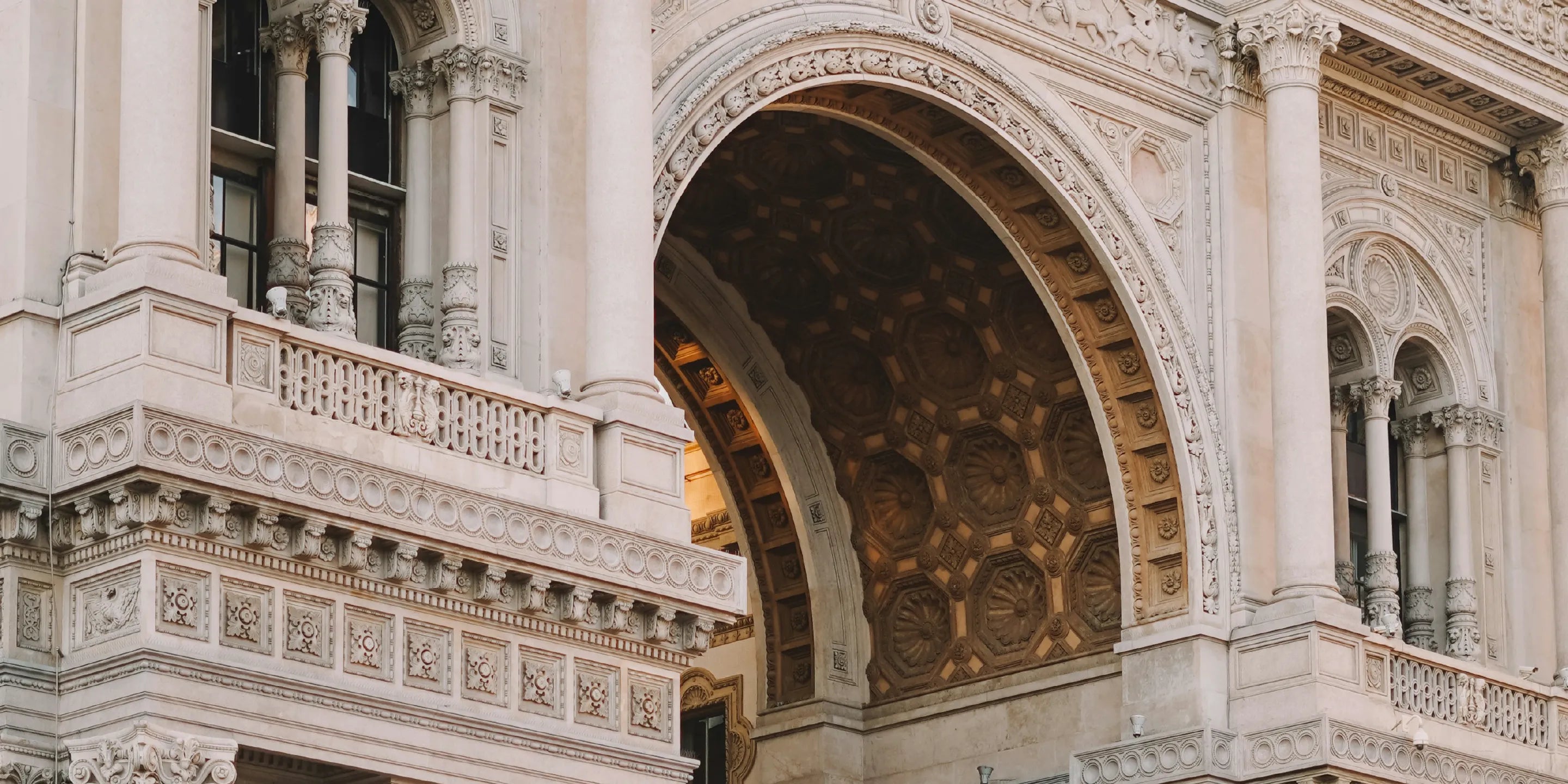 Close-up architectural detail of a grand neoclassical building facade with ornate stone carvings, columns, windows, and a large arched interior opening.