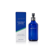 A cobalt blue glass room spray bottle with a black spray top stands next to its blue and white packaging box. The box features the brand name 'capri BLUE' and the scent 'COCONUT SANTAL'.
