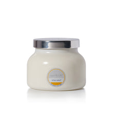 A small jar candle with an off-white body and a shiny silver lid, featuring a circular label that reads 'capri BLUE VOLCANO'.