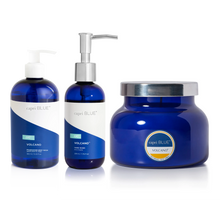 Three Capri Blue Volcano beauty and home products on a white background: a body wash bottle, a hand wash pump bottle, and a candle.