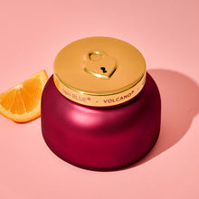 Red candle with gold lid and 'Volcano' branding on a pink background