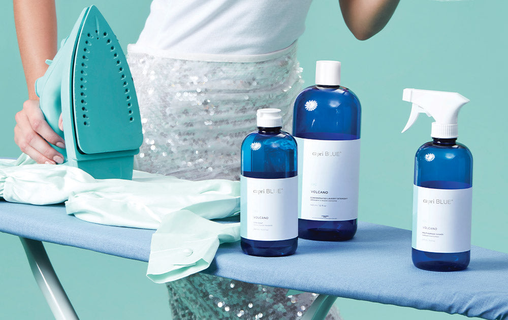 Various capri BLUE laundry products on an iron board next to a shirt and a woman holding the iron