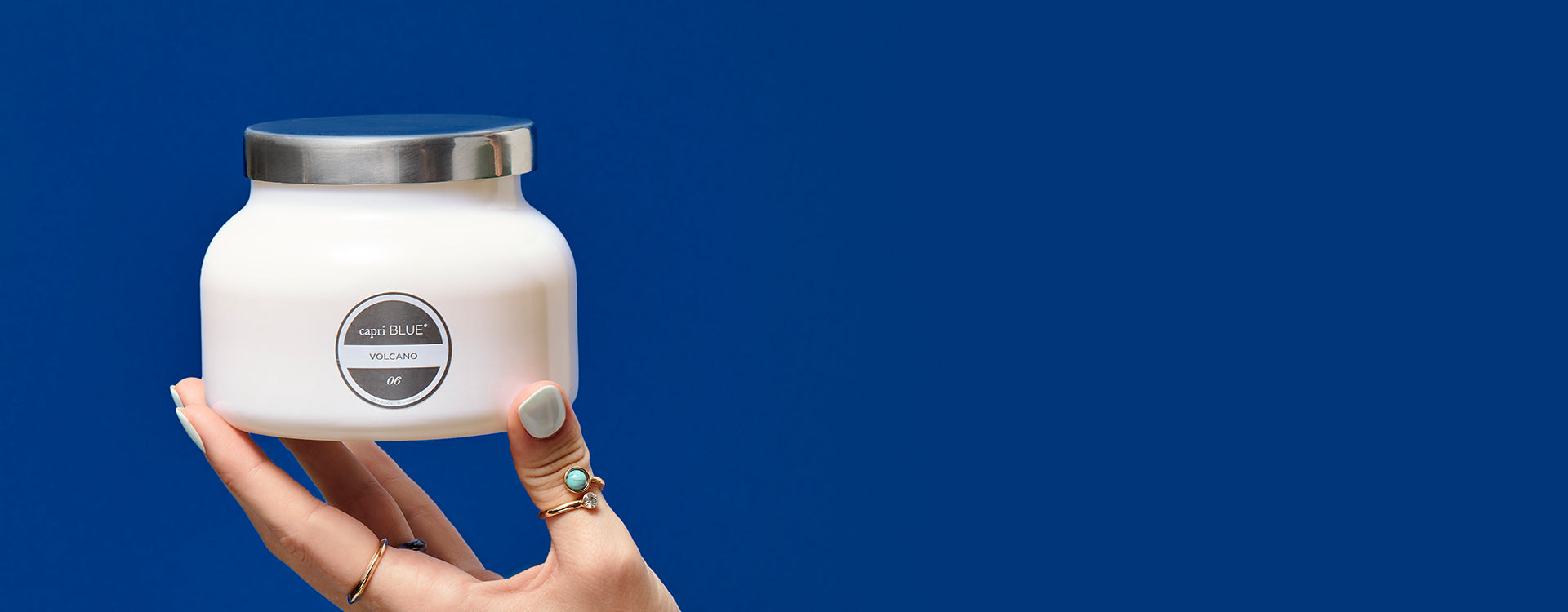 Hand holding a Volcano White Signature Candle on a blue background